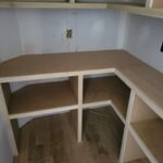 Custom built-in bookcase with face-frame shelving and countertop work surface, raw wood finish ready for paint.