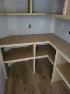 Unfinished corner closet desk and open shelving in raw wood, ready for finish