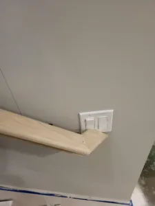 Unfinished wood handrail with a curved return end, descending toward a wall-mounted switch plate
