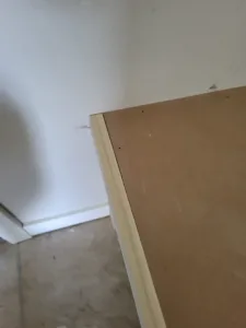 Unfinished shelf panel with a white edge band, viewed from below in a corner