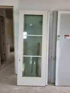 White pre hung door with frosted glass lites leaning in a hallway under construction.