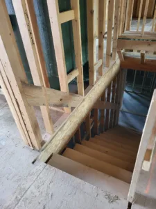 Open riser staircase framed within stud walls, stringer brace and sheathing visible, rough construction.