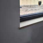 Finished wood window sill installed at interior window opening, painted drywall surround.