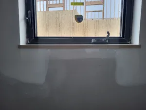 Wood window sill installed below a black framed window, exposed stud framing visible outside