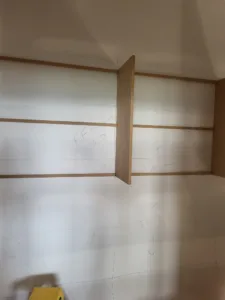 Pencil layout marks and a vertical divider panel positioned on drywall, during closet shelf layout.