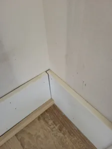 Wood shoe molding installed at the base of painted baseboard on a wood floor, inside corner.
