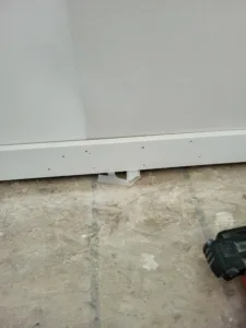 White baseboard installed on OSB subfloor with a white plastic bracket at its base