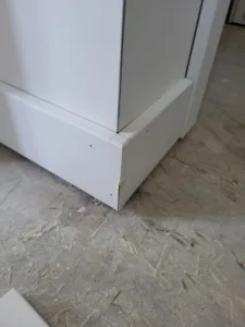 Painted baseboard trim wraps an outside corner, meeting a wood subfloor before flooring install.