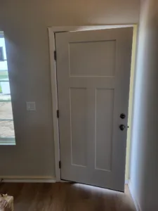 Painted three-panel door with white casing and black hinges installed in finished opening.