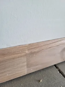 Raw wood baseboard installed at wall to floor junction, unpainted and ready for finishing.