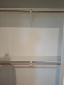 Closet shelf and wood hanging rod installed on white support brackets, mostly empty closet.