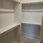 Walk-in closet with two-tier shelving and hanging rods installed, primed/painted walls ready for finish.