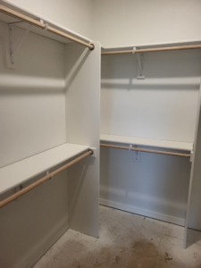 Walk-in closet with two-tier shelving and hanging rods, painted white with wood rod supports