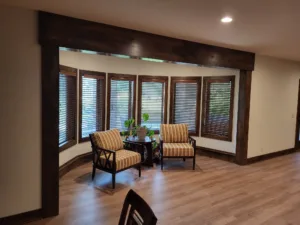 Finished sunroom with dark wood cased windows, blinds, and seating arranged along the curve.