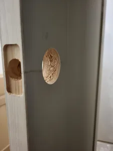 Door edge with two drilled holes for lockset hardware prep, edges rough and splintered