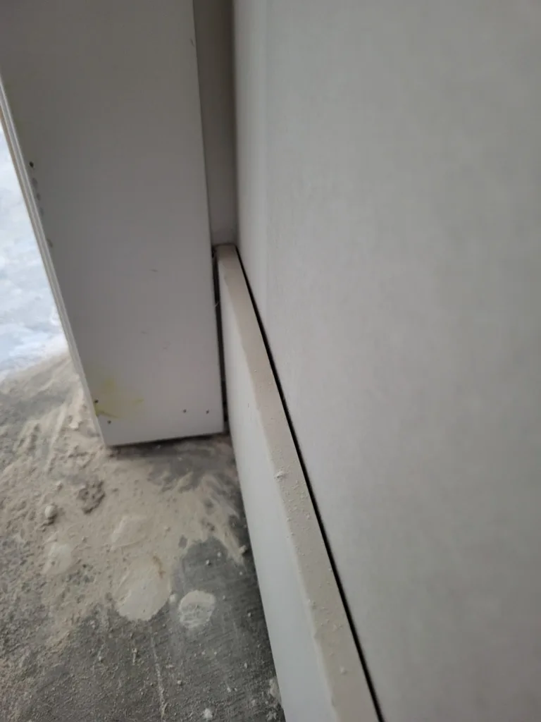 Side view of white baseboard with a visible gap between its top edge and the wall, beside door casing.