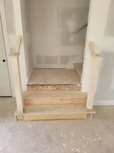 Two step landing at the bottom of an interior stair with square newel posts and rough rail pieces on each side