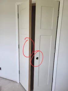 White bifold closet doors open, showing an interior hinge and a hole bored for hardware