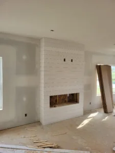White shiplap fireplace surround with firebox opening cut in, room still at drywall stage