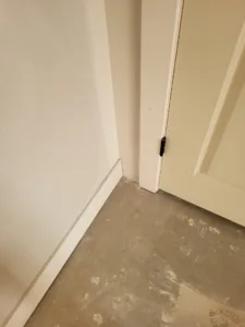 Painted door edge beside baseboard trim along the wall, concrete subfloor visible.