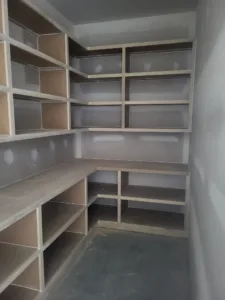 L-shaped built-in closet shelving with open cubbies and a counter shelf, drywall still unfinished.