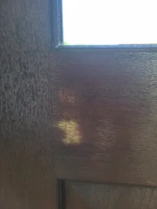 Stained wood door frame corner joint with visible wood grain texture, daylight visible above
