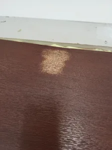 Dark stained wood surface meets a white trim piece with adhesive at the seam.