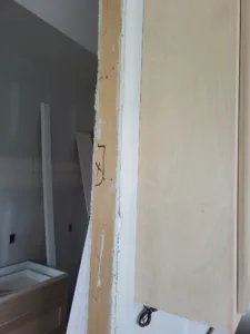 Corner with a raw wood jamb and painted gray wall, casing not yet installed, framing stage.