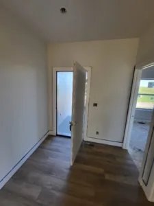 Open white door leading to a bright exterior space, hallway with vaulted ceiling and wood look flooring