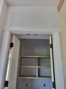 Painted closet doorjamb and casing with black hinges installed, small cubby shelving visible inside.