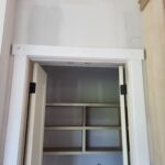 Painted closet opening with jamb and casing installed, ready for bi-fold or bypass door slabs. Interior shelving visible.