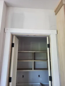 White painted door open into a closet with a small interior shelving grid visible in the background.