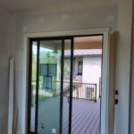 Black aluminum sliding patio door with white interior casing and jamb extensions installed in opening.