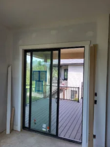 Black-framed sliding patio door with white interior casing installed, manufacturer labels still on the glass.