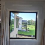 Fixed window with black frame and white casing installed in interior wall opening, ready for paint.