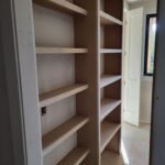 Raw wood shelving installed in closet—multiple shelves on cleats, unfinished, ready for paint.
