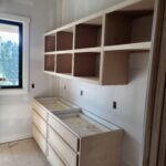 Custom built-in bookcase with face-frame cubby shelving and drawer base, raw wood ready for paint.