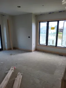 Finished drywall room with wood window casing and baseboard installed, trim lumber staged on the subfloor