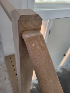Unfinished wood handrail fitted to a beveled post top, with drilled holes visible on a board below