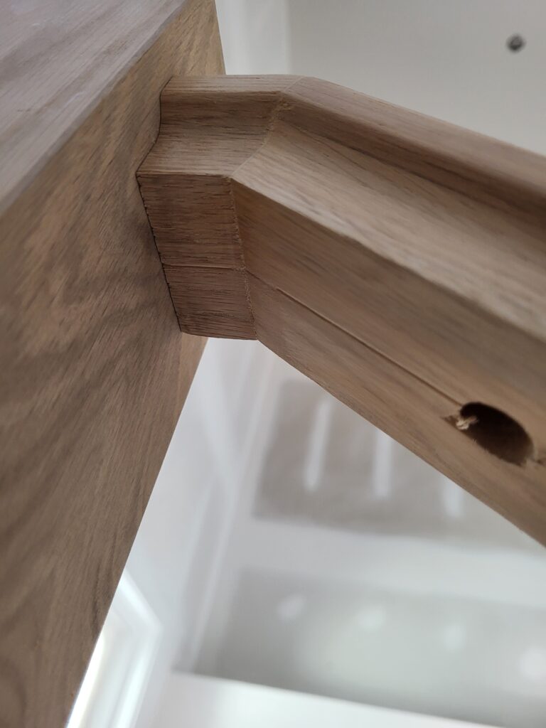Mitered outside corner on unfinished oak trim carpentry, front edge of the joint closed tight with no visible gap