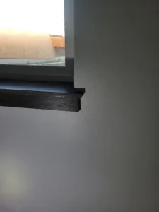 Installed dark stained wood window stool projecting into room, painted wall surrounding the window.
