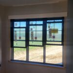 Large multi-pane window installed in rough opening with jamb extensions and drywall surround, pre-casing stage.