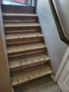 Narrow interior stairwell with raw wood treads, old fasteners and adhesive residue, ready for refinishing.