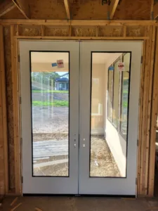 Black-framed French doors with full glass lites installed in a rough framed opening, framing stage.