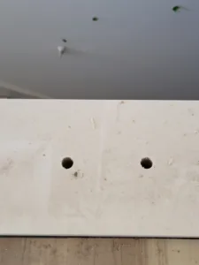 White backer board mounted to a wall with two drilled mounting holes visible.
