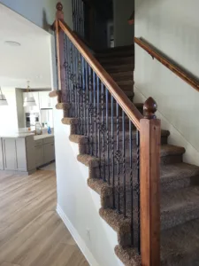 Finished staircase with wood handrail, ornate vertical iron balusters, and carpeted treads