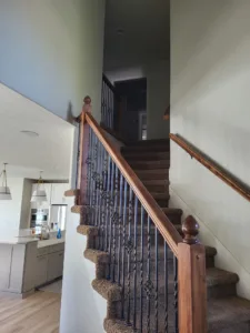 Finished staircase with wood newel post, ornate vertical iron balusters, and carpet treads