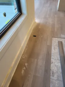 Painted white baseboard installed along wood flooring beside an exterior window casing