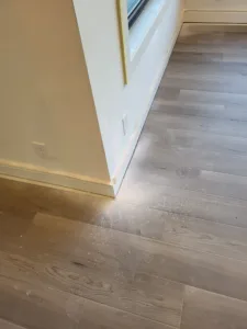 Incorrect: white baseboard along a room corner near an opening, wood look flooring below