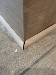 Raw wood shoe molding installed at the base of a wood-toned baseboard, meeting the floor.